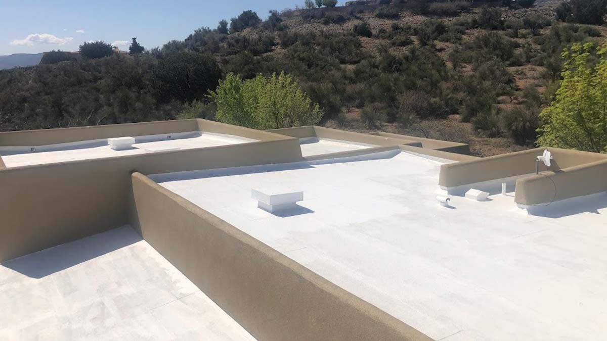 White-coated flat roof with tan parapet walls, surrounded by hills and trees.