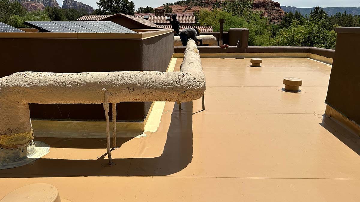Flat roof with tan coating and large insulated pipe, surrounded by low walls.