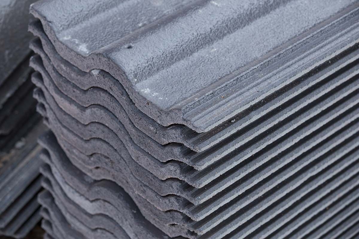 Stack of gray, textured roof tiles with curved edges.