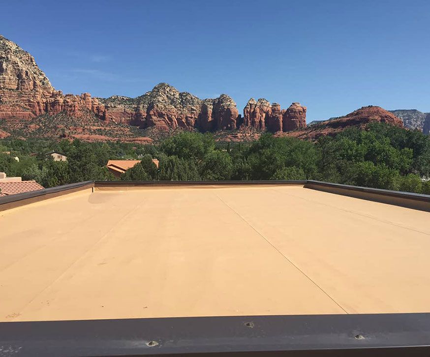 View from a roof of red rock mountains and green trees under a blue sky.