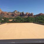 Flat, tan roof with a backdrop of red rock formations and green trees under a blue sky.