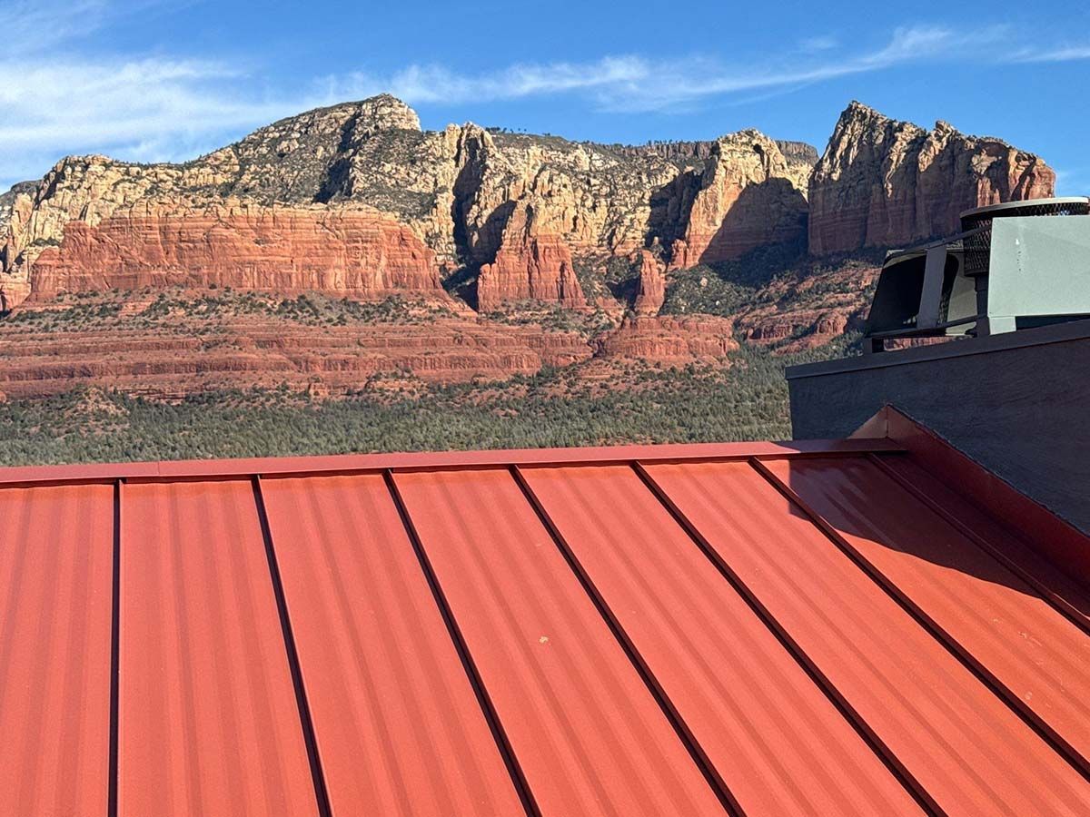 Red metal roof with mountain backdrop under a blue sky.