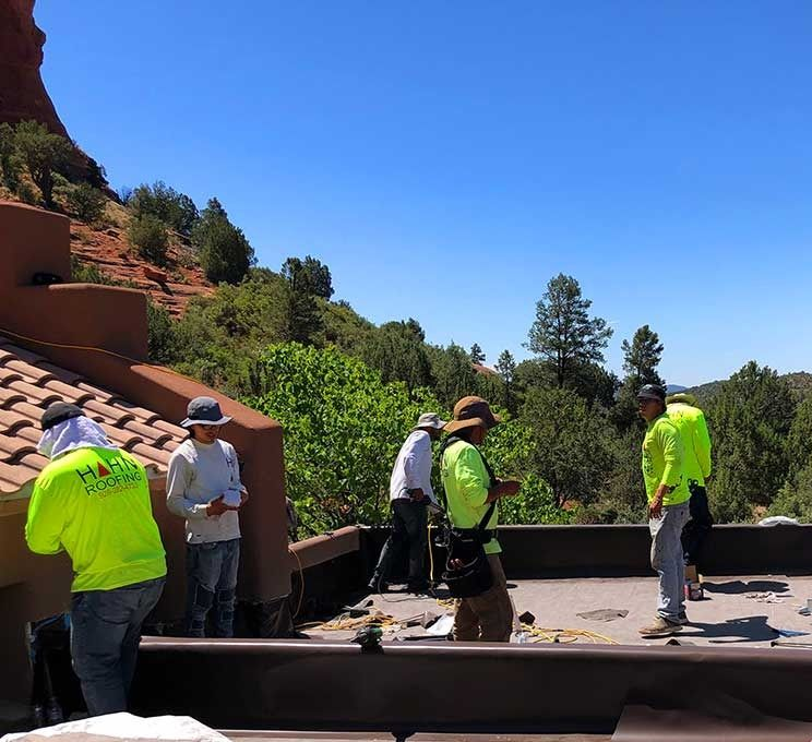Workers on a rooftop in bright green safety vests, with a mountain backdrop.
