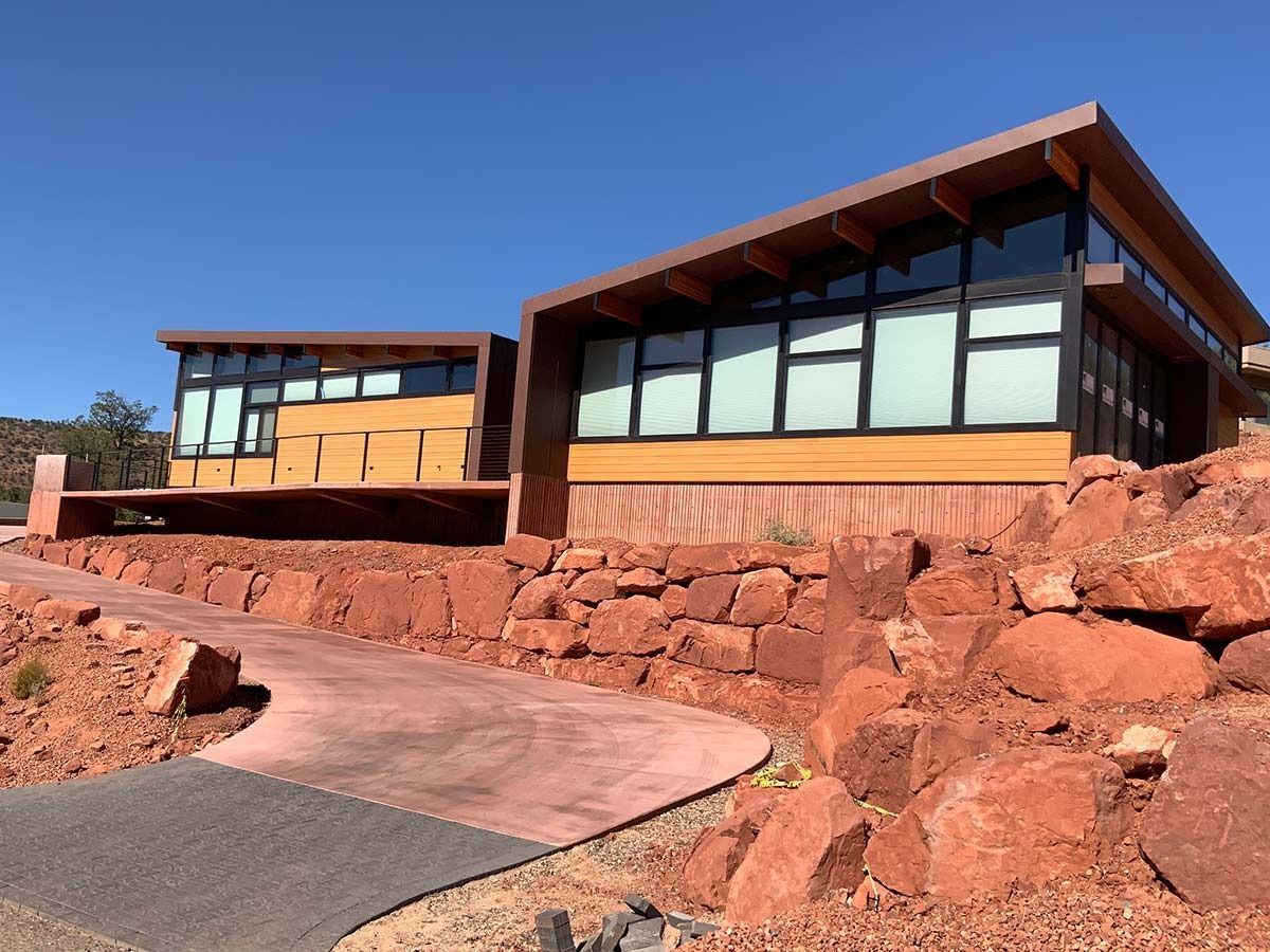 Two modern buildings with large windows, built into a red rock hillside, with a walkway.