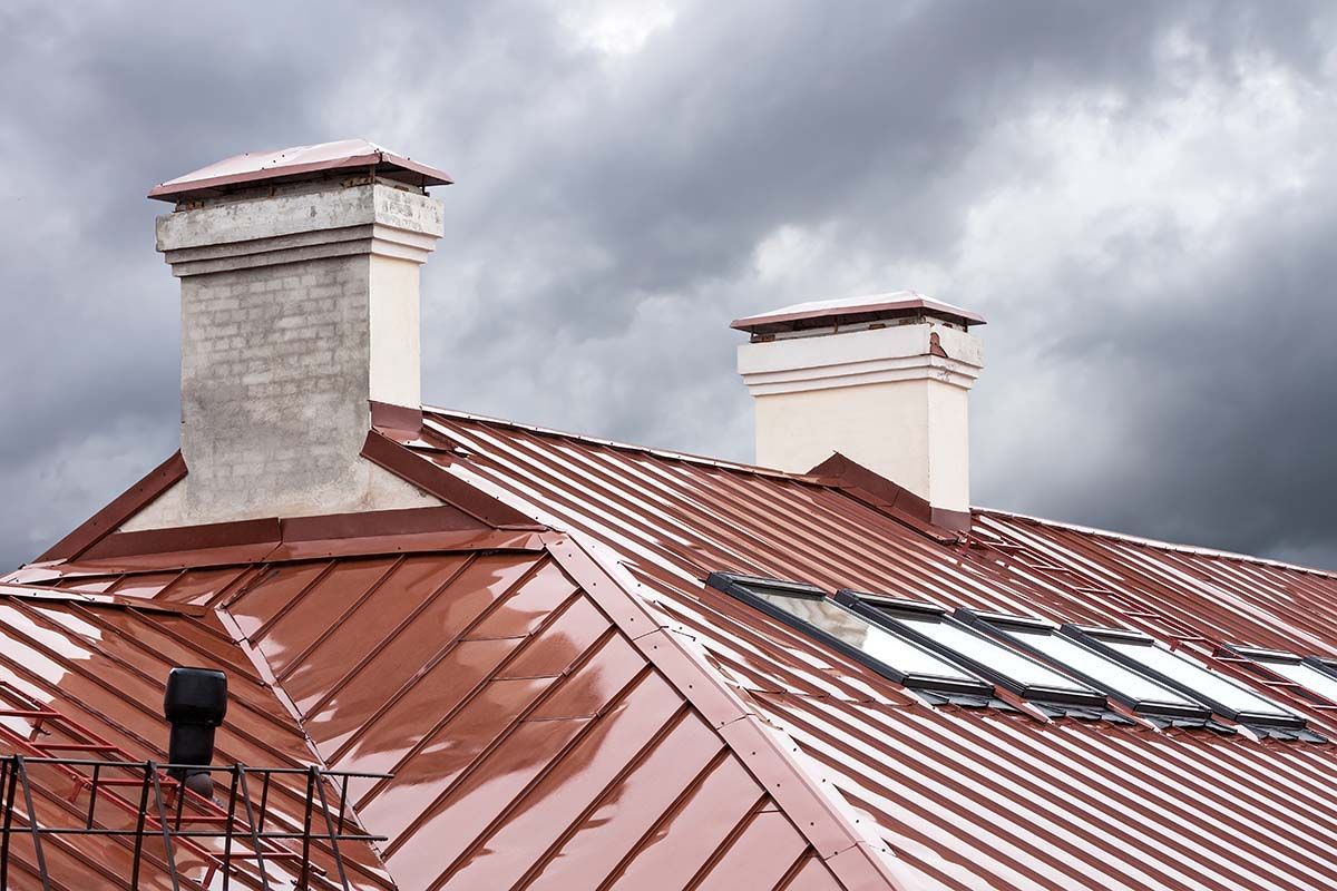 Red metal roof with two chimneys against a cloudy sky.