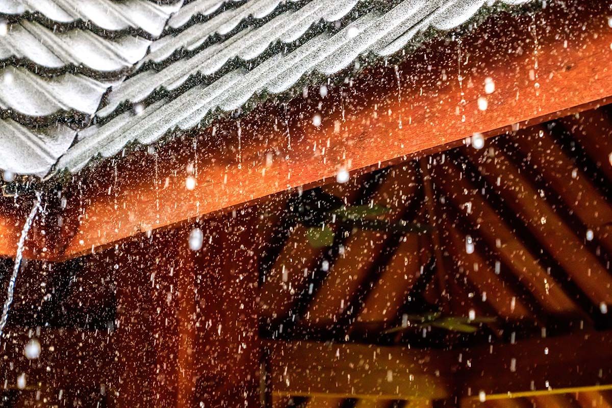 Rain pouring from a brown roof. White tiles, droplets.
