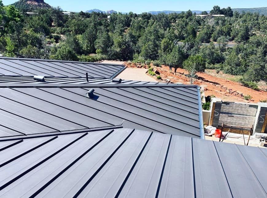 Dark metal roof with parallel lines, scenic trees, and red rock landscape.