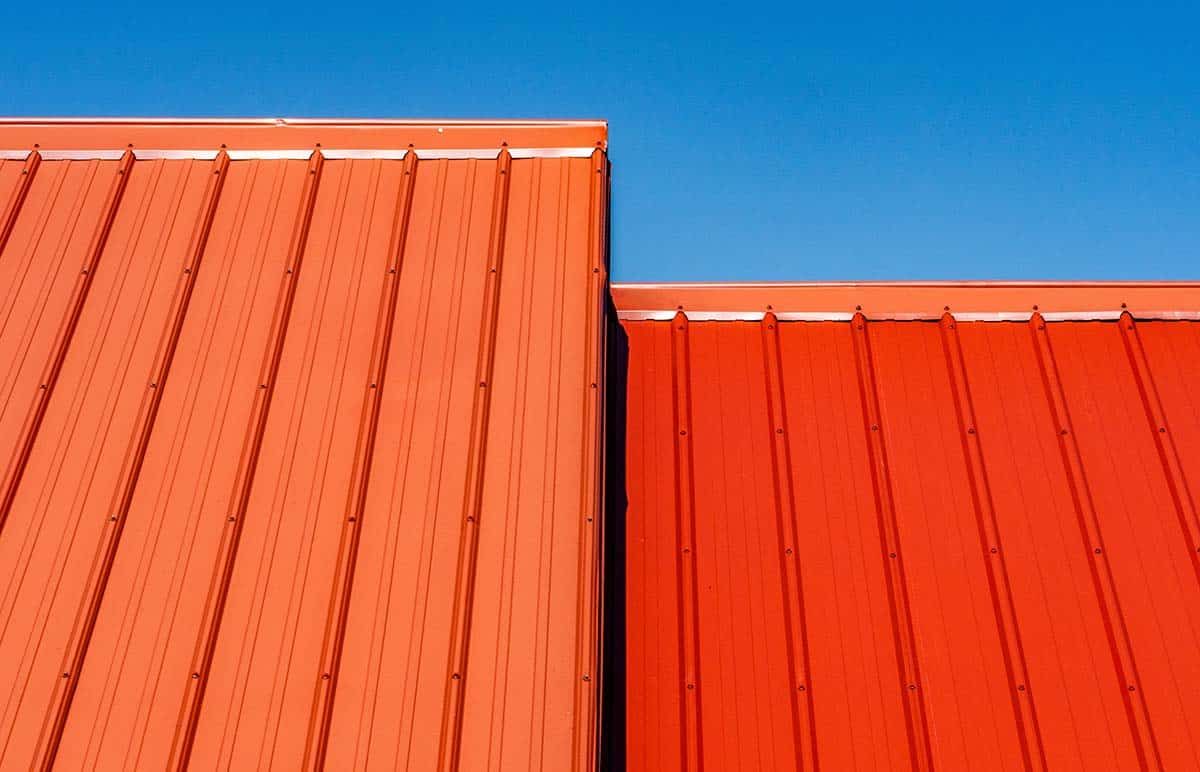Two sections of a red metal roof against a clear blue sky.