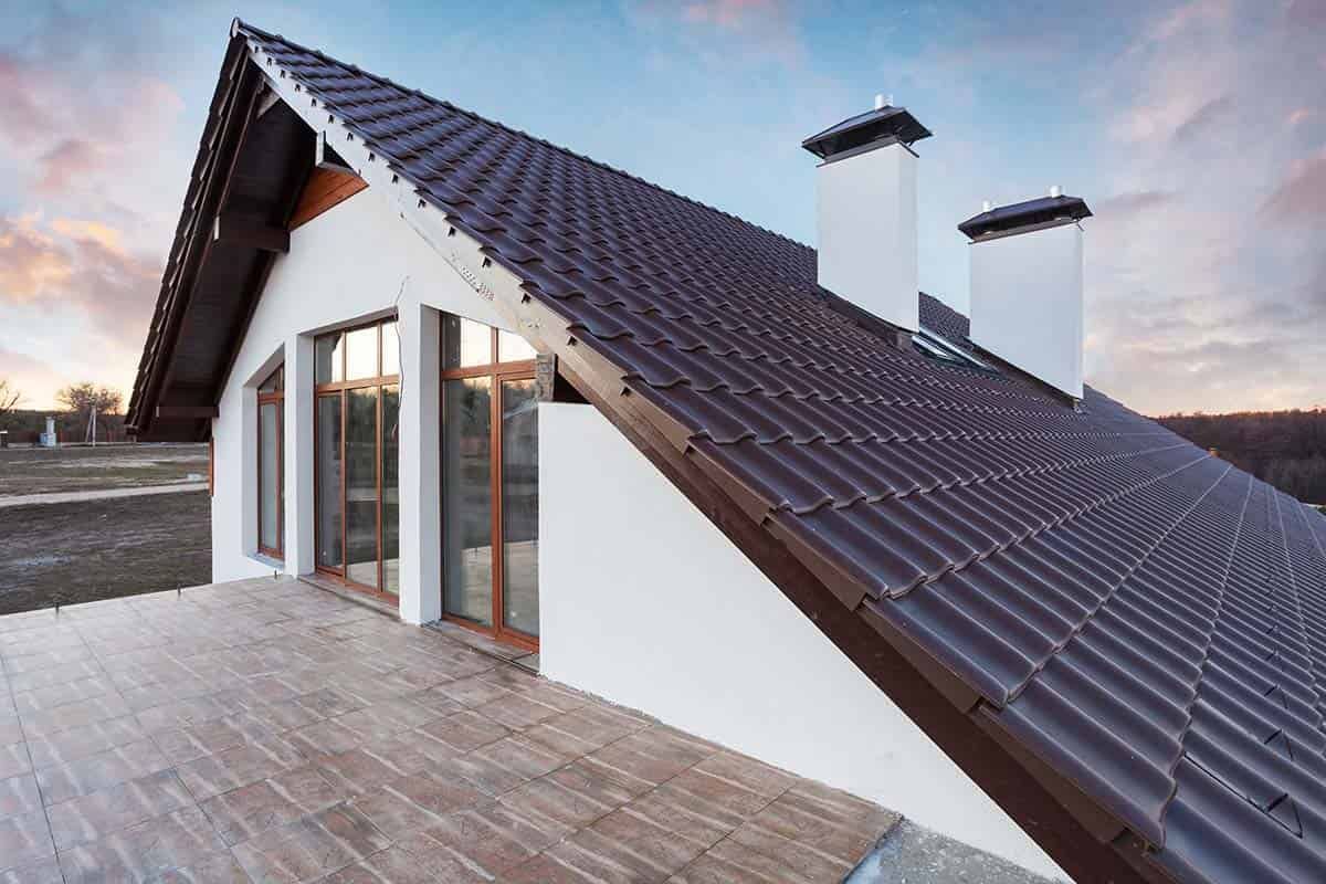 White house with brown roof and two white chimneys, overlooking wooden deck, dusk sky.