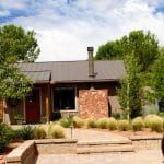 Small brown house with red door, stone facade, gray roof, and landscaping.