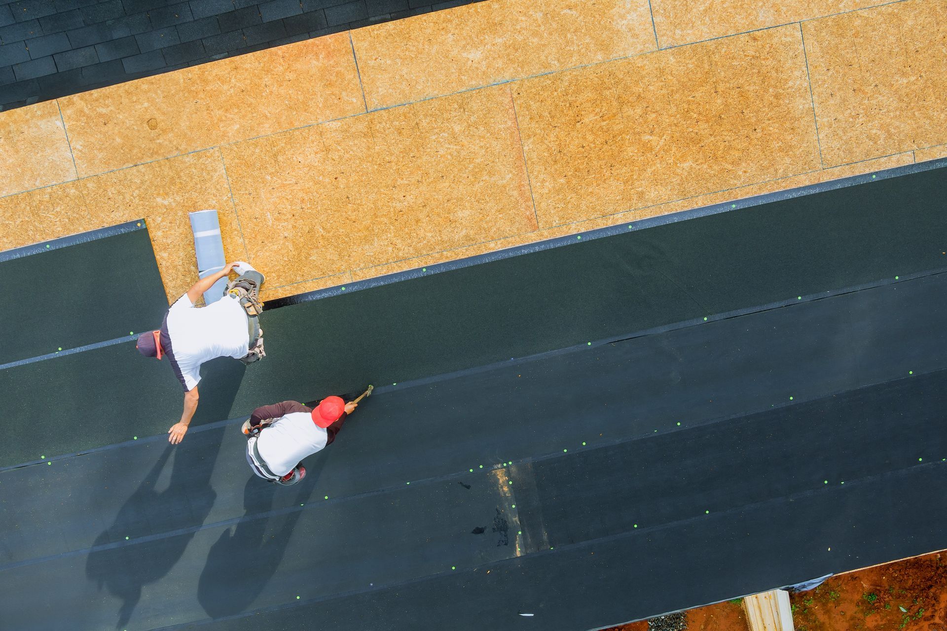 Two roofers installing roofing material on a building's roof.