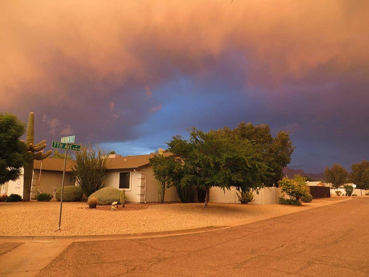 A house on a street with a reddish-brown sky and contrasting blue patch; likely a dust storm.
