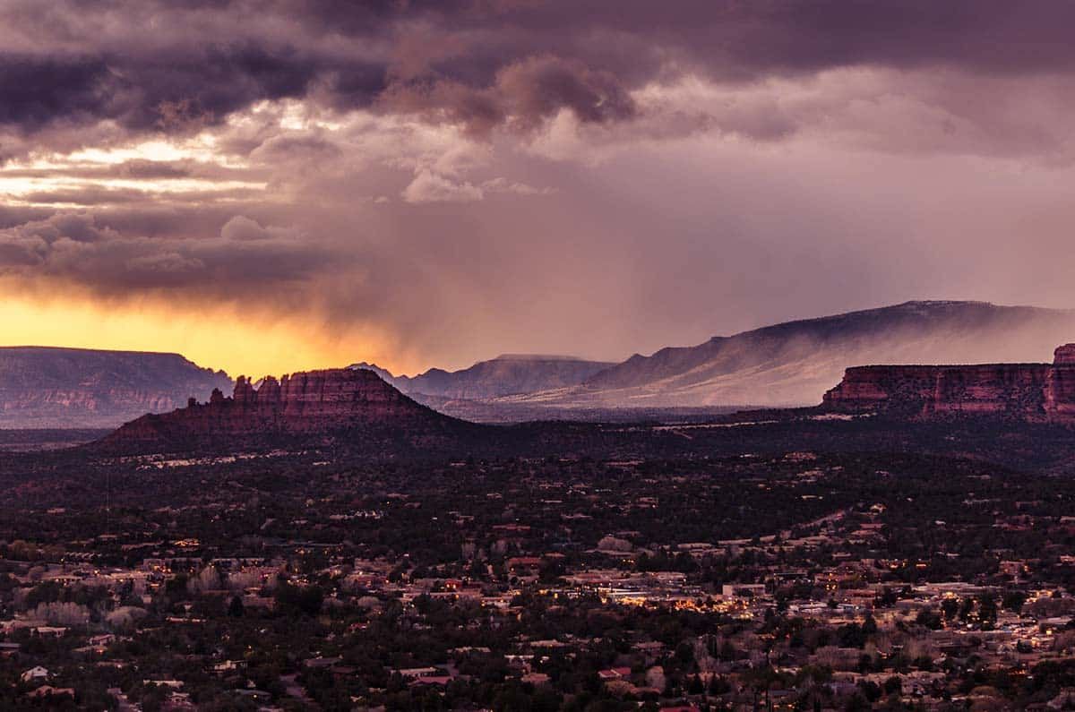 Dramatic sunset over a mountainous landscape with dark clouds, casting shadows over the town below.
