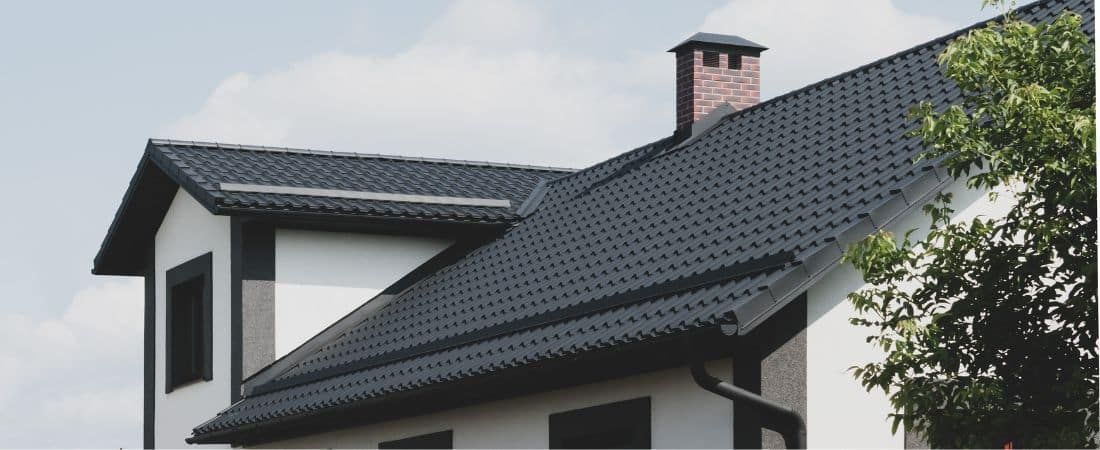 House with a dark roof and a brick chimney against a cloudy sky.