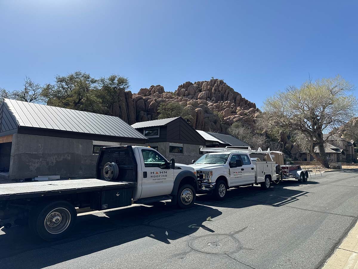 Flatbed truck towing a white truck and trailer on a street with buildings and a rocky mountain backdrop.