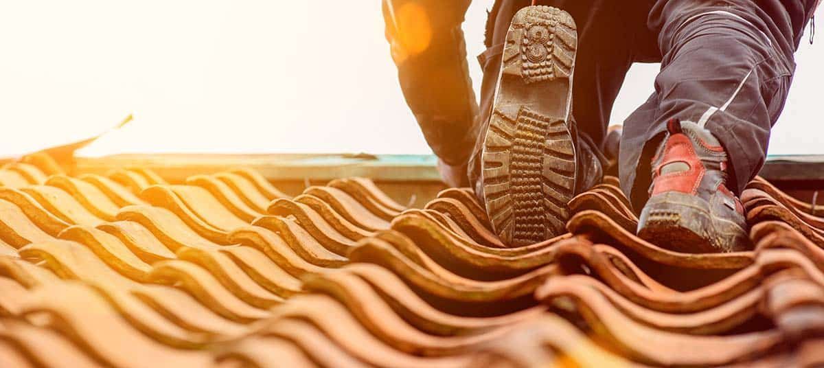 A person on a tiled roof, visible are their boots and legs, with a bright sky in the background.