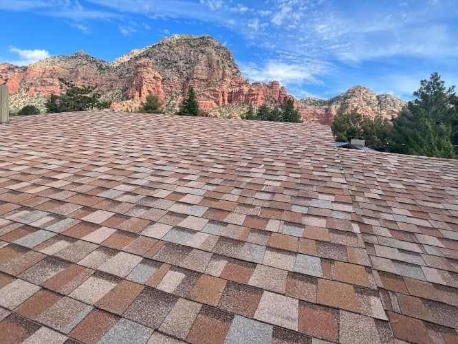 View of a multi-colored shingled roof with red rock mountains and blue sky in the background.