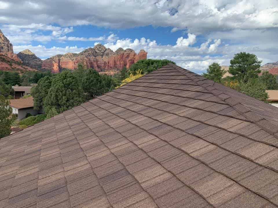 Brown shingled roof with a scenic backdrop of red rock formations and a cloudy sky.
