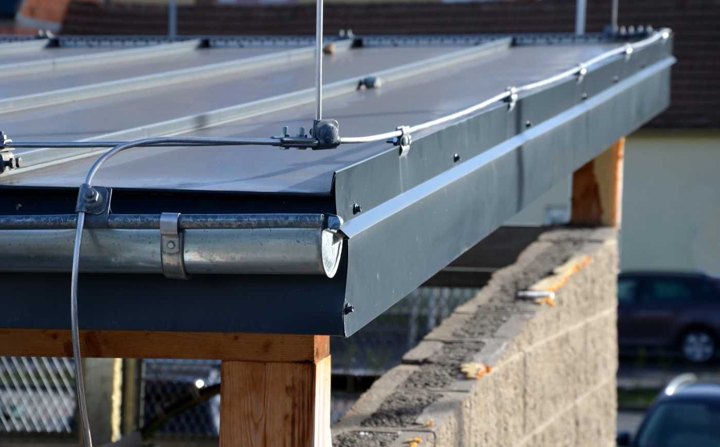 Close-up of a metal roof edge with a gutter, attached to a wooden and brick structure.
