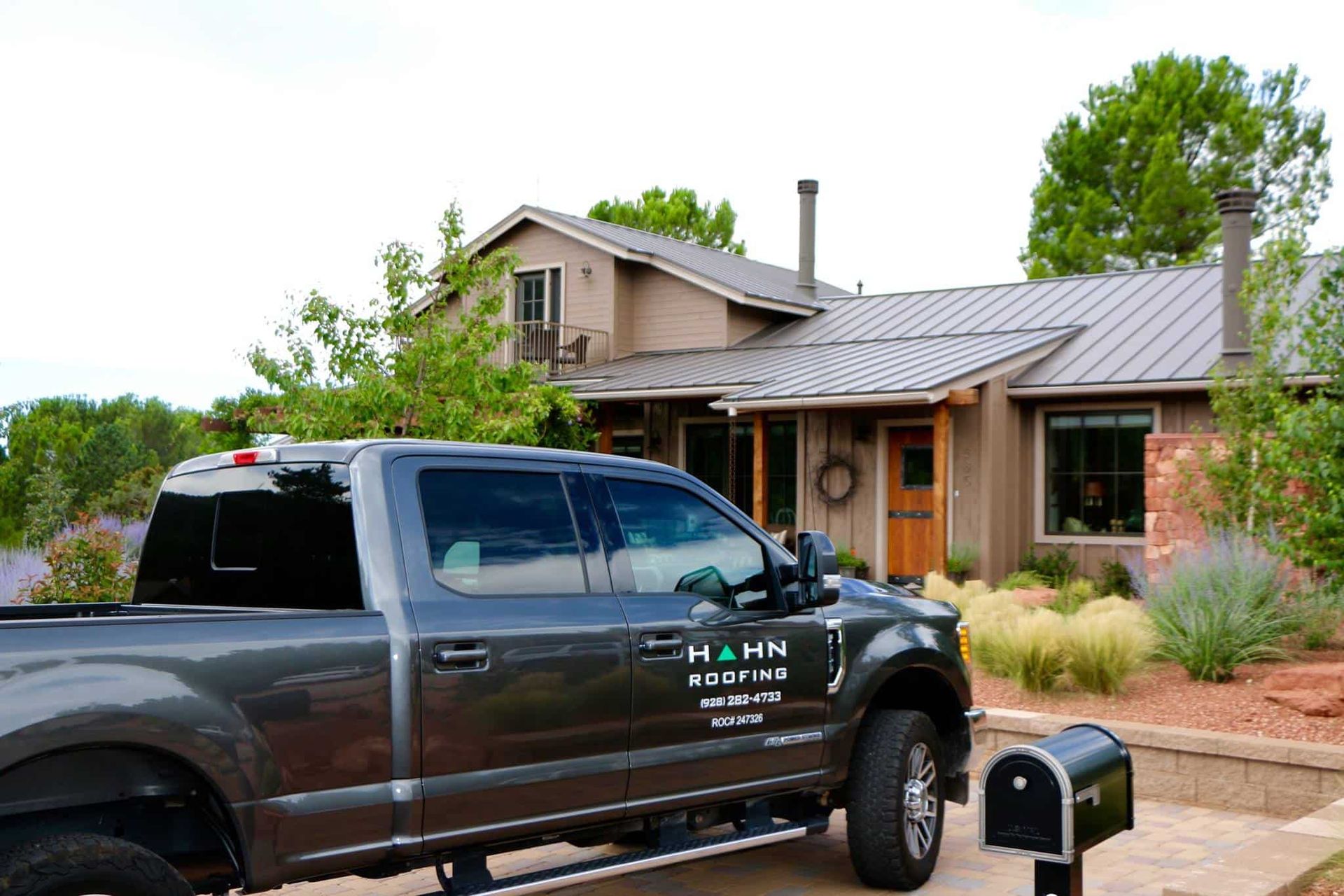 Gray pickup truck parked in front of a house, advertising Hahn Roofing.