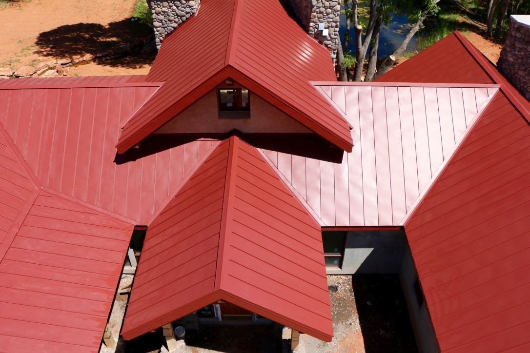 Red metal roof of a building with multiple angles and a chimney.
