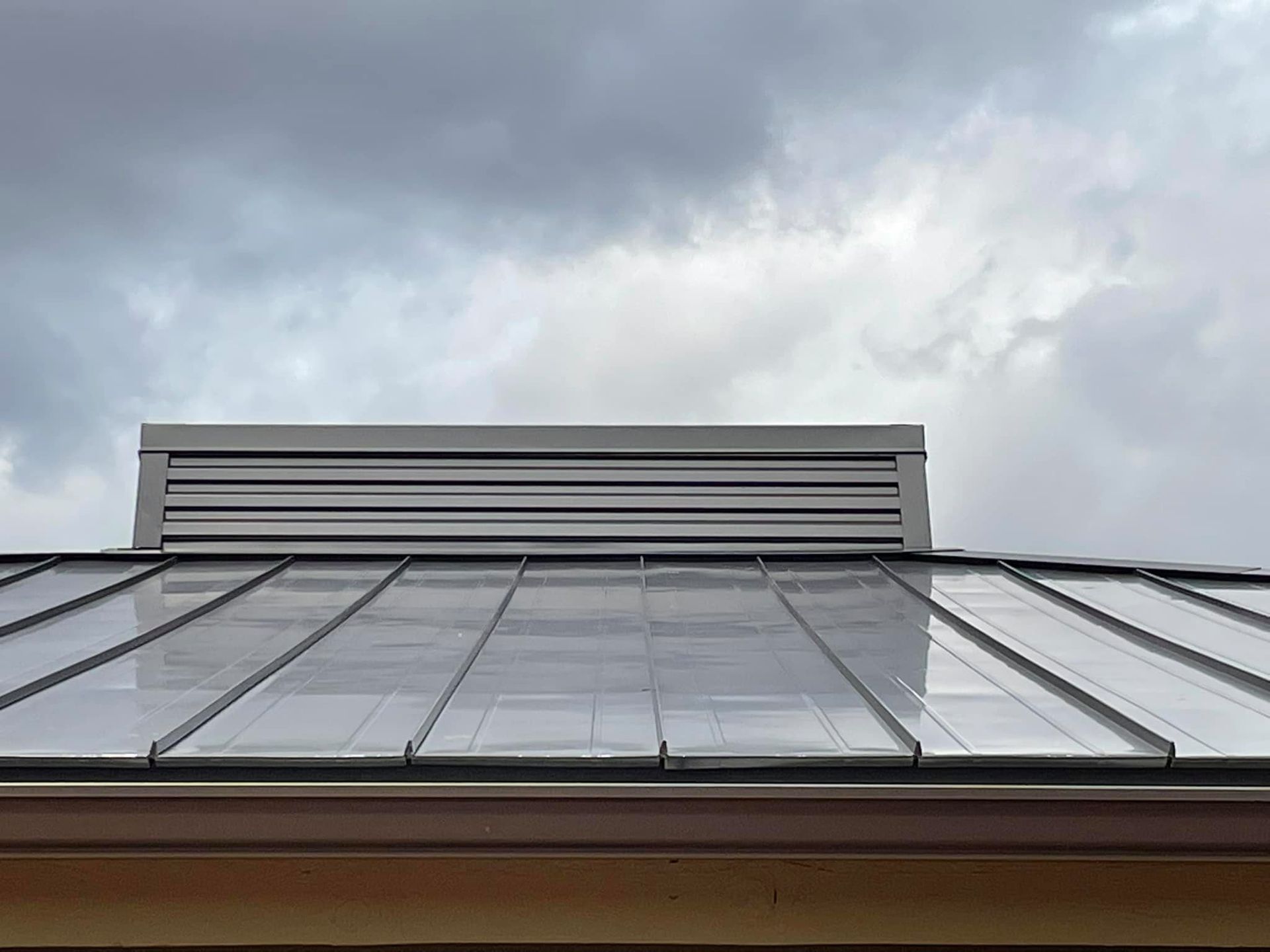 Metal roof with vent against a cloudy sky.