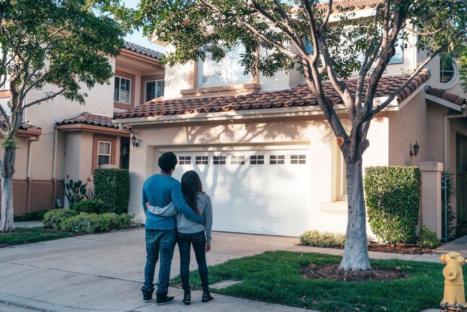 A man and a woman are standing in front of a house.