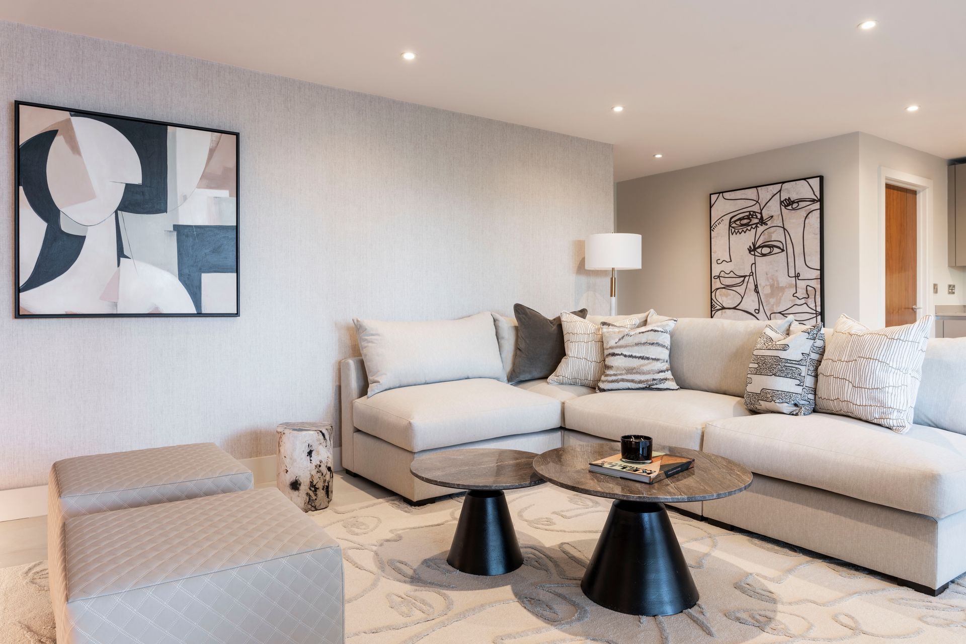 Modern living room with beige sectional sofa, abstract wall art, and two black side tables
