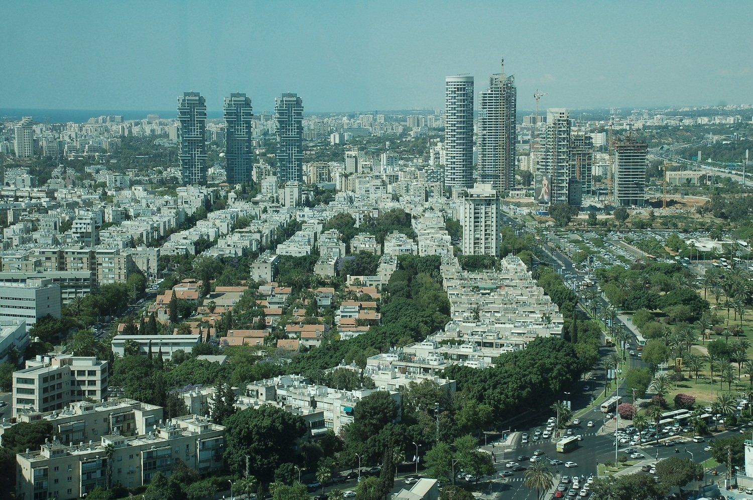 נוף עירוני של תל אביב עם גורדי שחקים מודרניים ובניינים ישנים יותר, רחובות וירק תחת שמיים כחולים.