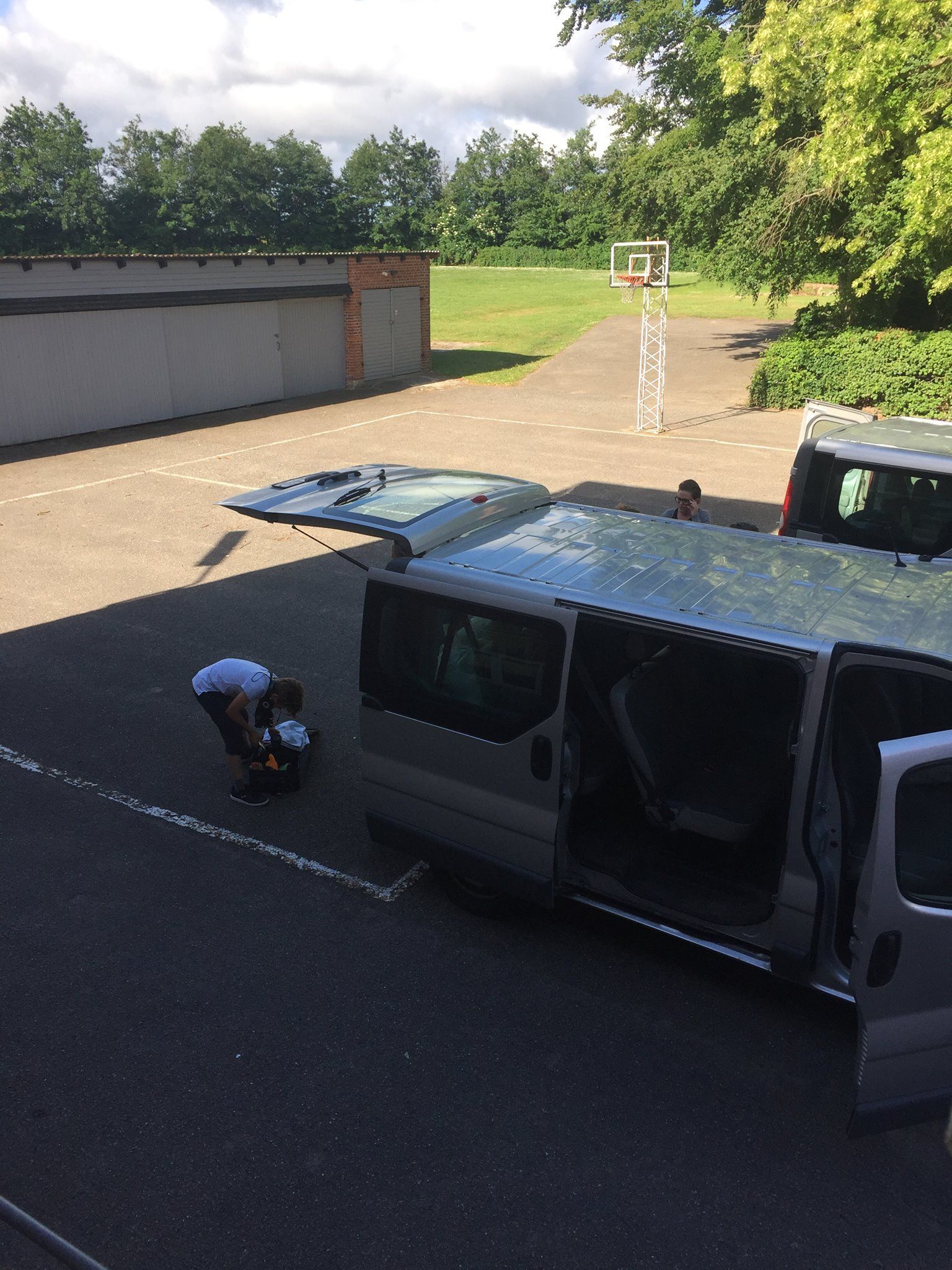 Person, der læsser udstyr ind i en varevogn parkeret på en asfaltplads nær en basketballkurv.