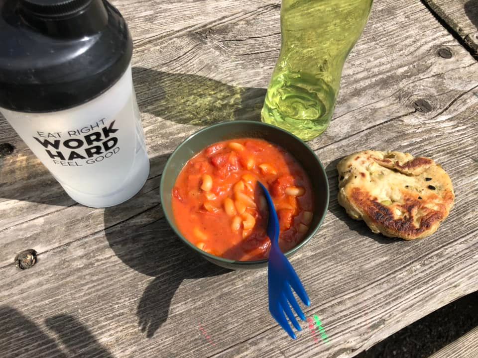 Skål med bønner, brød, vandflaske og glas på et træbord.