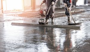 Workers smoothing wet concrete on a floor in a bright indoor construction site