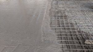 Wet concrete being poured beside a metal rebar grid on a construction site