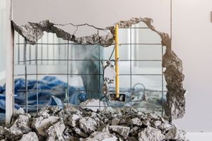Collapsed wall with rubble and exposed pipes inside a room, with a blue tarp and yellow ladder visible inside.