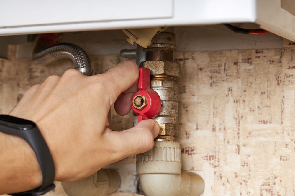 Person's Hand Turning a Red Valve on a Pipe Connected to a Boiler — B&A Plumbing and Gas In Wauchope, NSW