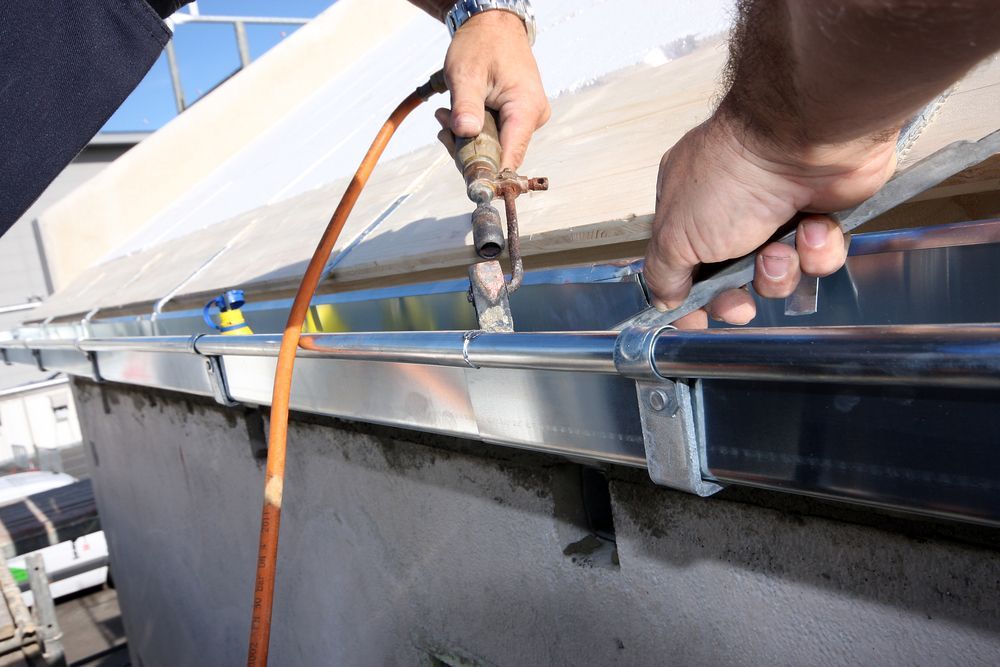 Person Attaching a Pipe to a Gutter With a Wrench Outdoors — B&A Plumbing and Gas In Wauchope, NSW