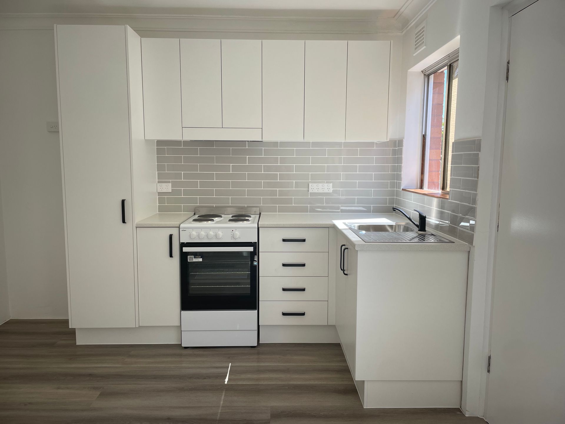 A modern white kitchen with wood-look flooring, subway tile backsplash, a stove, and a sink — B&A Plumbing and Gas In Wauchope, NSW
