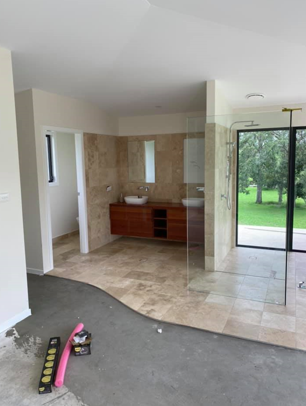 A bathroom under renovation featuring a vanity with two sinks, tile flooring, a glass shower, and concrete floor space  — B&A Plumbing and Gas In Wauchope, NSW