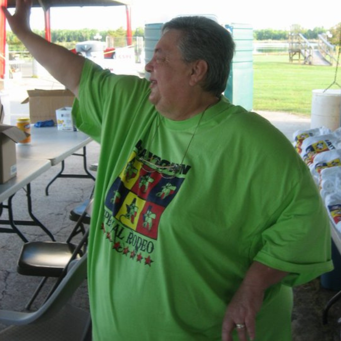 Man in a bright green T-shirt raising one arm at a picnic shelter table outdoors