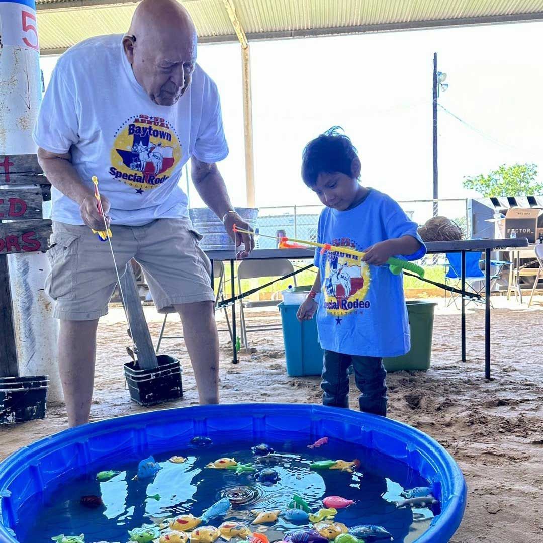 An adult and a child fishing for plastic toys in a blue kiddie pool filled with water during the Baytown Special Rodeo.