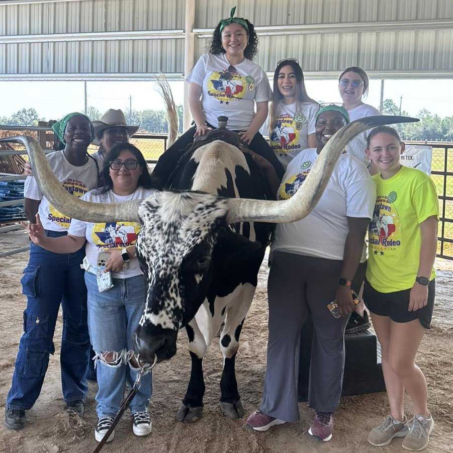 A group of young people posing with a longhorn steer, one person sitting on its back. Everyone is wearing Baytown Special Rodeo t-shirts.