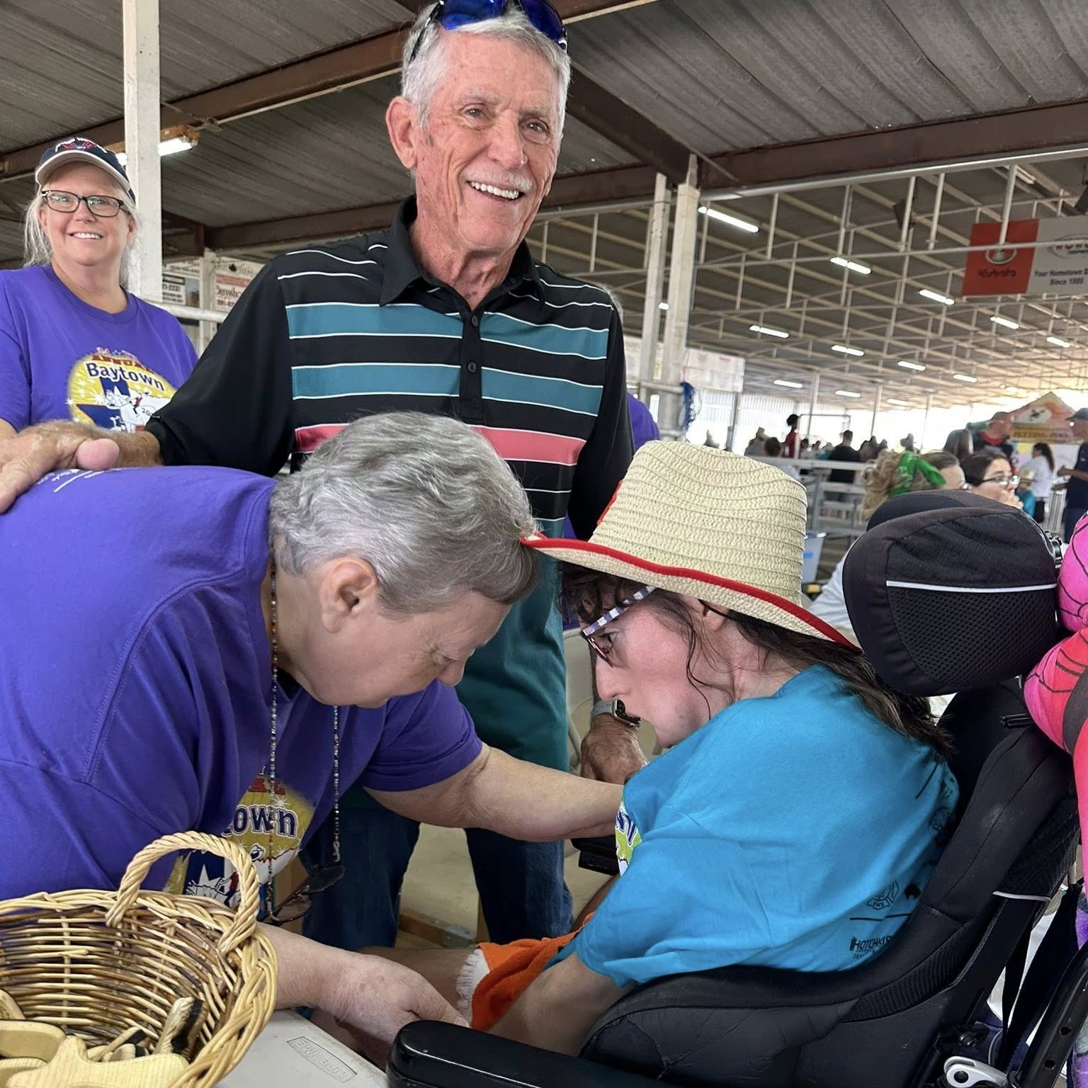 A man in a striped shirt smiles as two people in purple shirts and one in a blue shirt interact with a person in a wheelchair during the Baytown Special Rodeo.