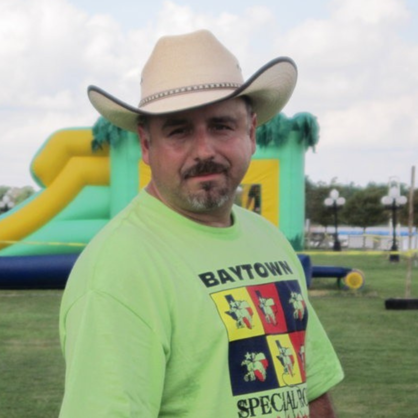 Man in cowboy hat and neon green Baytown Special shirt standing outdoors near an inflatable structure