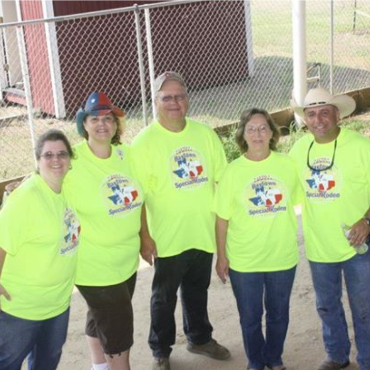 Five people in neon yellow shirts stand together outdoors in front of a chain-link fence.