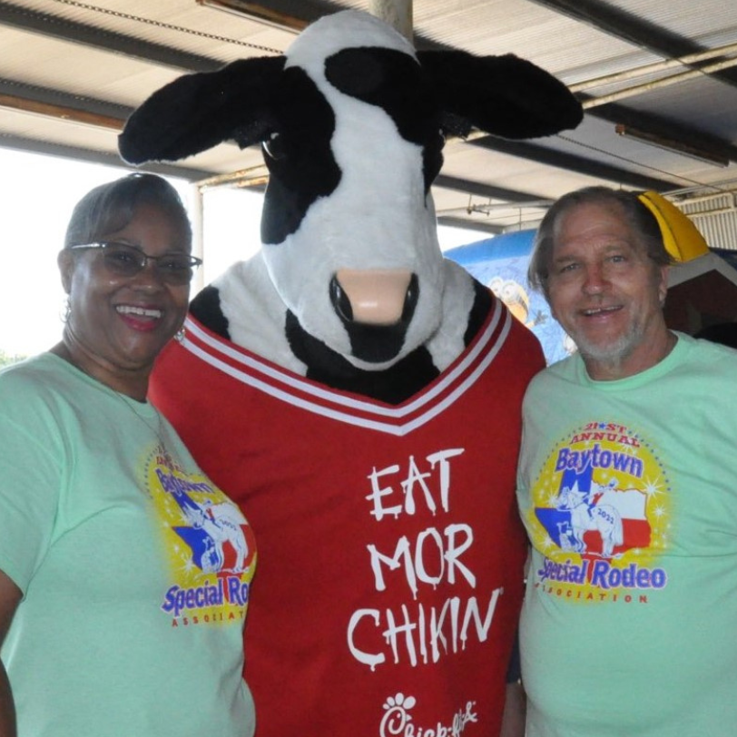 Two people posing with a cow mascot in a red “EAT MOR CHIKIN” shirt at a Special Rodeo event