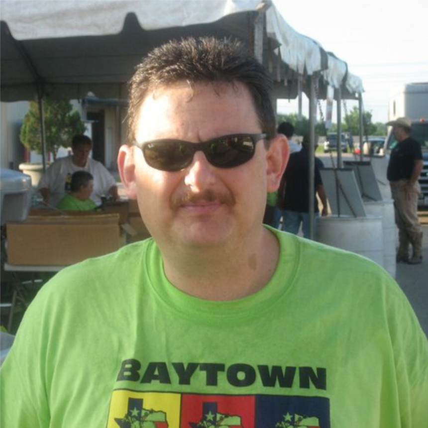 Man in sunglasses wearing a bright green Baytown shirt at an outdoor event under a canopy