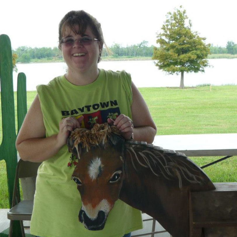 Woman in a lime green shirt posing with a carousel horse by a lakeside picnic shelter