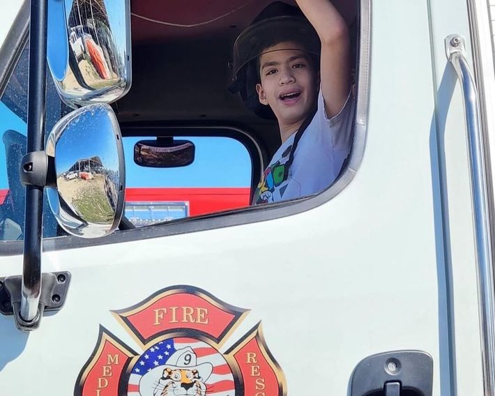 A child sits in the driver's seat of a fire truck, smiling and wearing a helmet, with a fire department emblem visible on the door during the Baytown Special Rodeo.