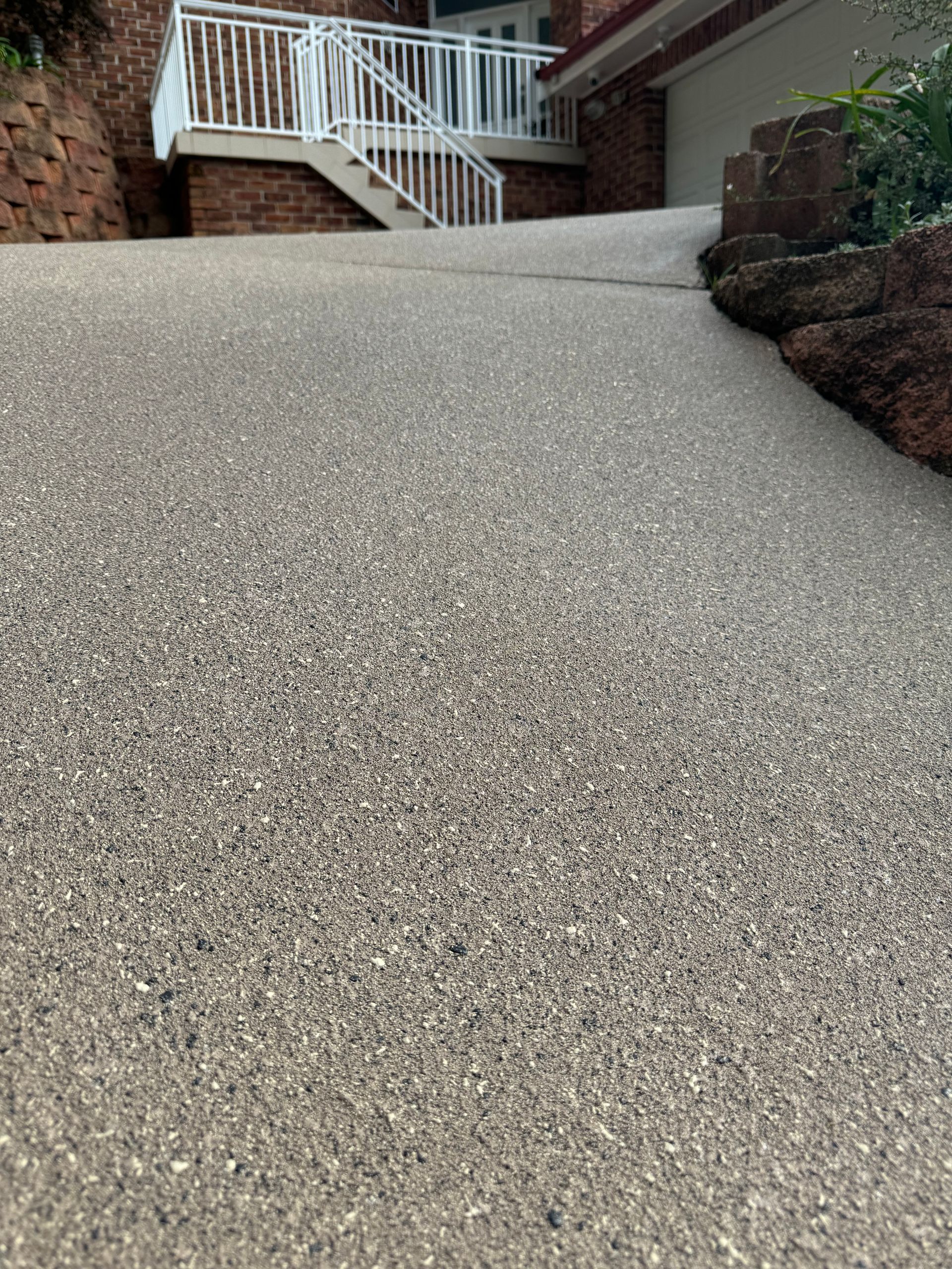A Man Is Standing in A Driveway Next to A Fence — Illawarra Resurfacing Pty Ltd in Balgownie, NSW