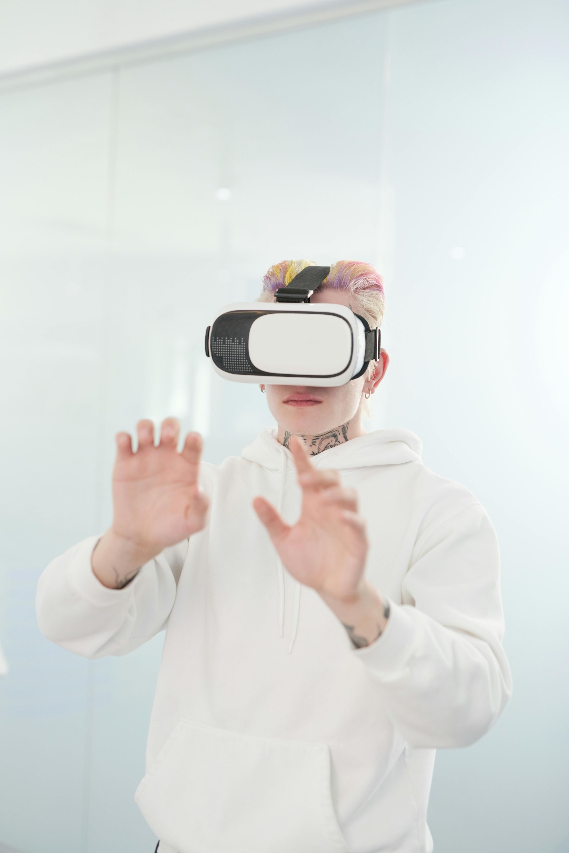 Person wearing a VR headset, hands raised, standing in front of a white wall.